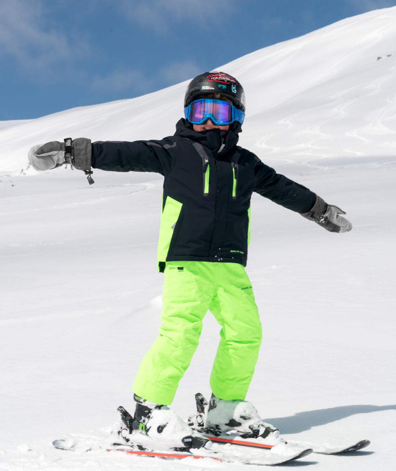 a kid skiing on a mountain in a black jacket with green and gray highlights