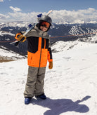 Person in ski orange beige and black jacket on a snowy mountain with a blue sky.