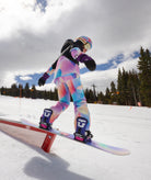 Person in colorful ski outfit performing a trick on a rail with trees and sky in the background