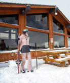 Person with skis standing outside a wooden cabin in the snow