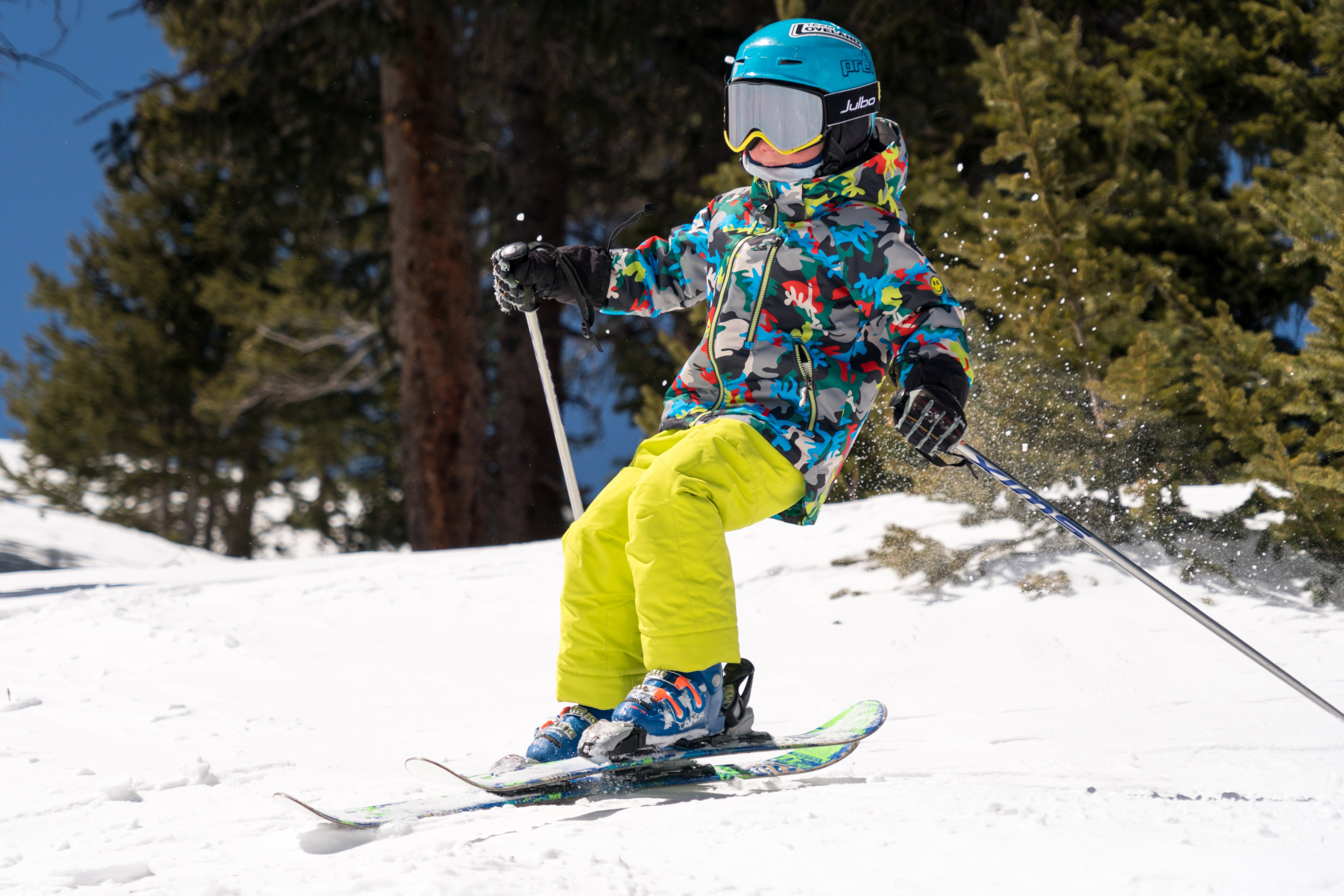 kid skiing on a snowy mountain wearing a multi colored patterned insulated jacket with hood